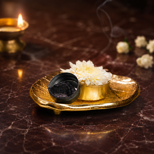 Aragaja Mai sacred kajal in black tin on a gold tray with brass diya lamp and jasmine flowers