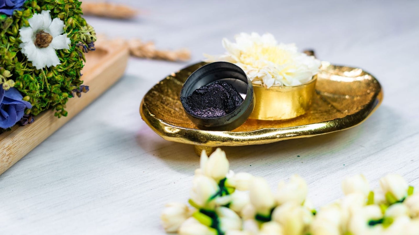 Open Aragaja Mai container showing the sacred black kajal texture on a gold tray with jasmine